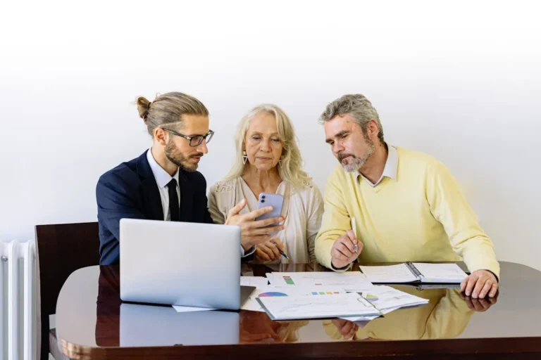 A lawyer discussing homeownership issues with an older couple at a table with documents and a laptop.