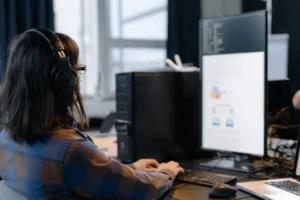 A woman wearing headphones working on a computer, focusing on secure identity management systems and interoperability.