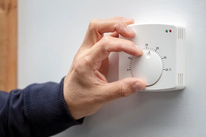 Why ECO4 Grants Are Perfect For Oil Boiler Replacement - Home Improvement - Next Magazine Hand adjusting a thermostat on the wall for temperature control.