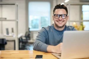 A smiling man using a laptop, representing user-friendly interfaces for decentralized identity management.
