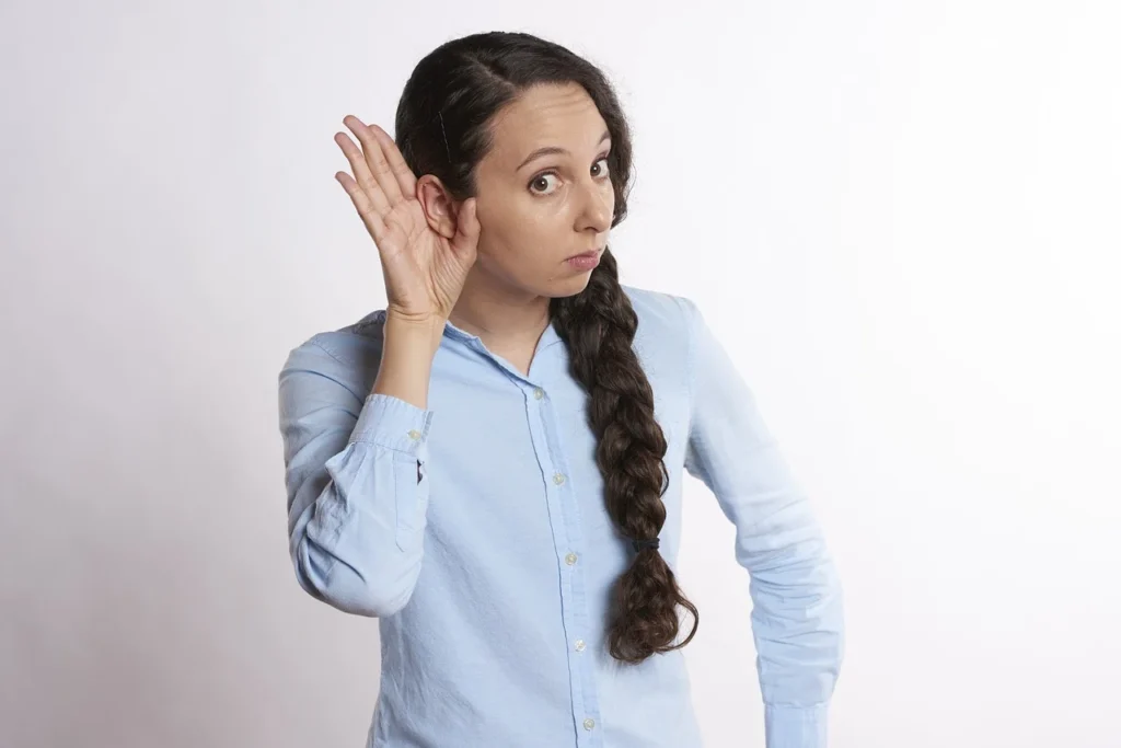 Woman listening intently with hand to ear, demonstrating the impact of improved acoustics.