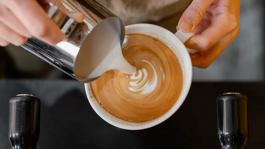 Barista pouring milk into a cup of coffee amidst rising coffee prices