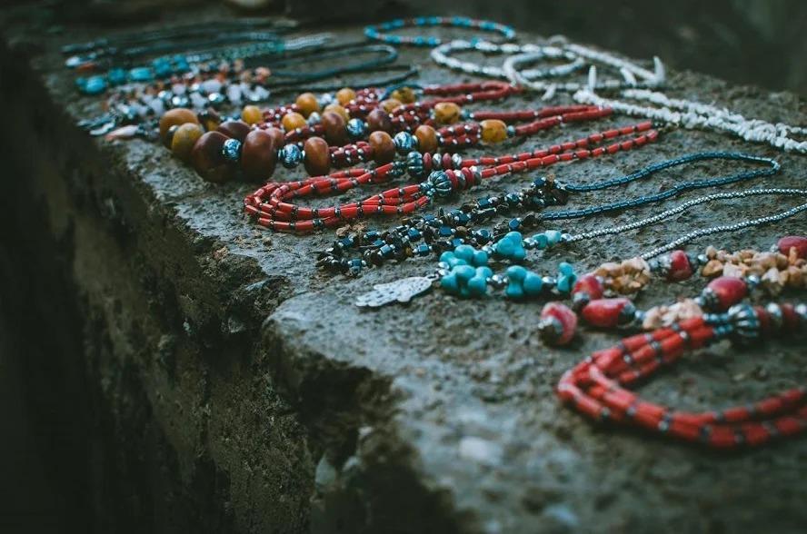 Handmade jewelry goods displayed on a stone surface, including colorful necklaces and beads.