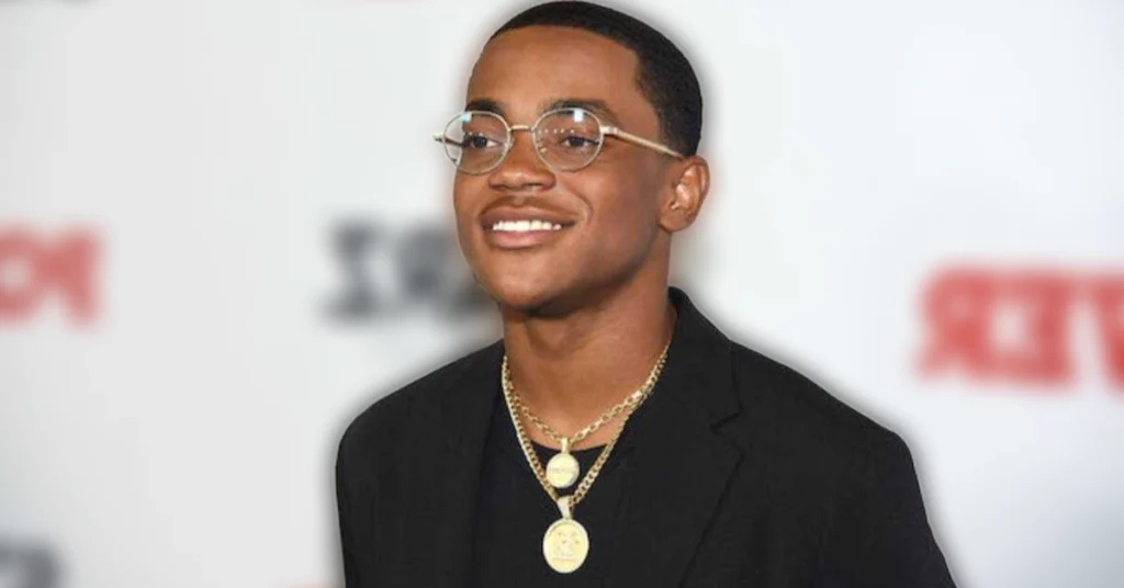 Michael Rainey Jr smiling at red carpet event wearing black suit and gold chains showing his $5 million net worth success
