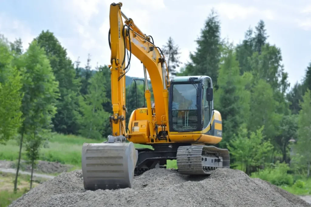 Excavator working on a gravel mound surrounded by trees, illustrating the challenges of Remote Construction Projects in isolated environments.