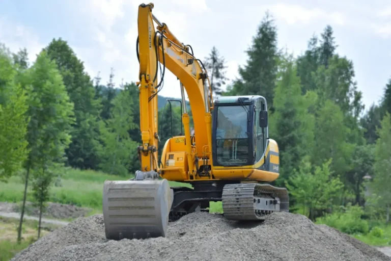 Excavator working on a gravel mound surrounded by trees, illustrating the challenges of Remote Construction Projects in isolated environments.