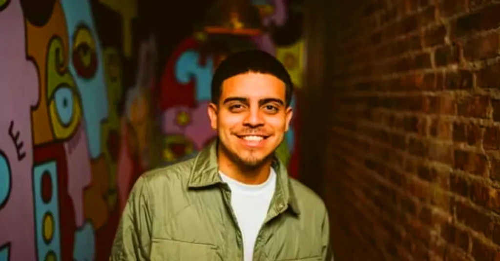 Ralph Barbosa smiling in green shirt at comedy club with colorful graffiti background